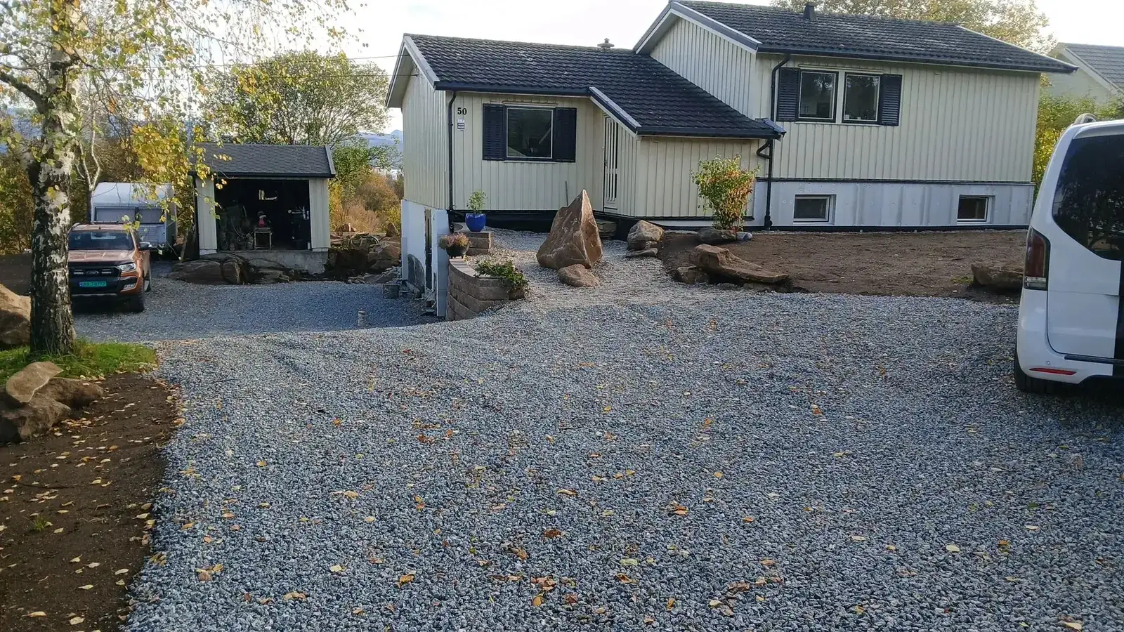 Ferdig opparbeidet uteområde med innkjørsel i knust stein, støttemur og natursteinparti foran boligen